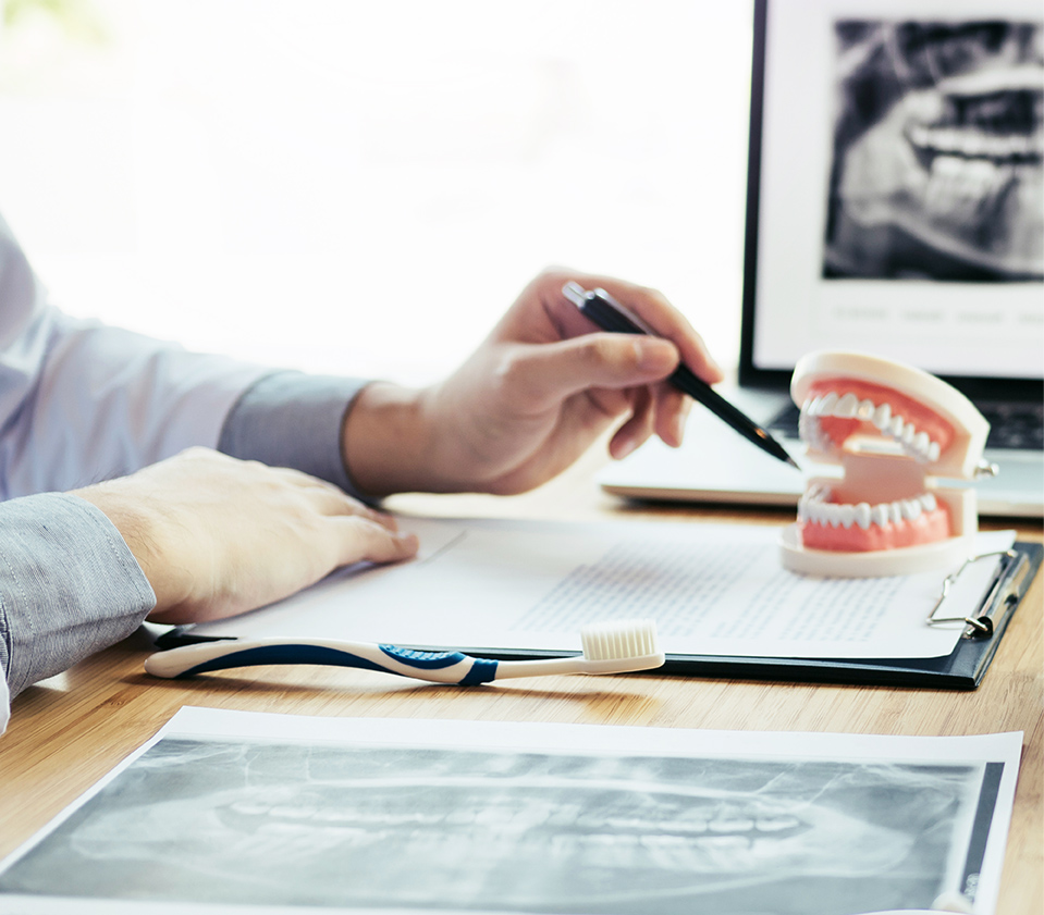 Dentist reviewing dental X-rays with model teeth on desk.